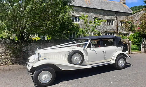 The Beauford convertible parked outside a stone cottage with white ribbons across the bonnet.