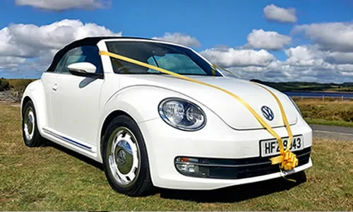 A white VW Beetle convertible with yellow bridal ribbons and bow on the bonnet.