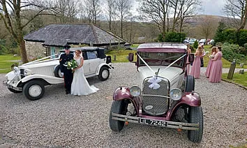 A bride and groom standing beside a vintage Bramwith with cream-and-burgundy livery.